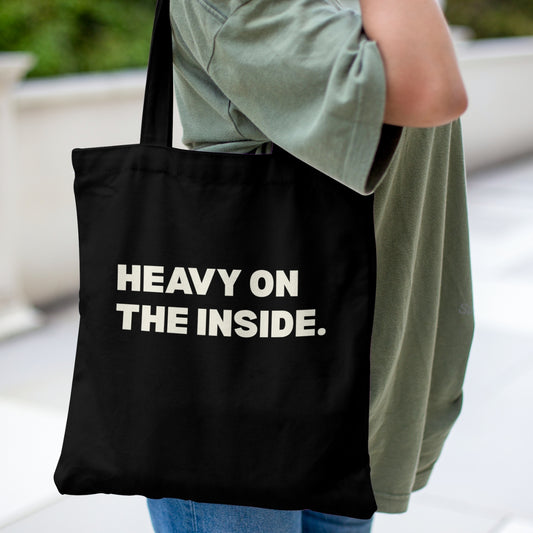 Black canvas tote bag featuring a bold Heavy on the Inside graphic